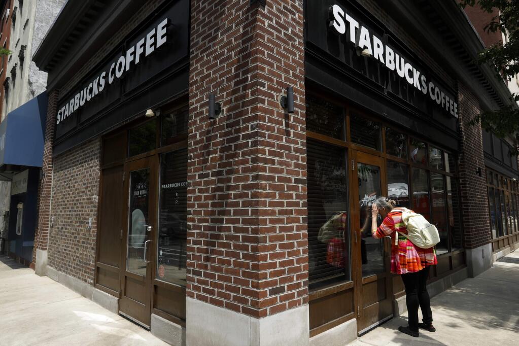 FILE- In this May 29, 2018, file photo a woman peers into a closed Starbucks Coffee shop in Philadelphia. (AP Photo/Matt Slocum, File)