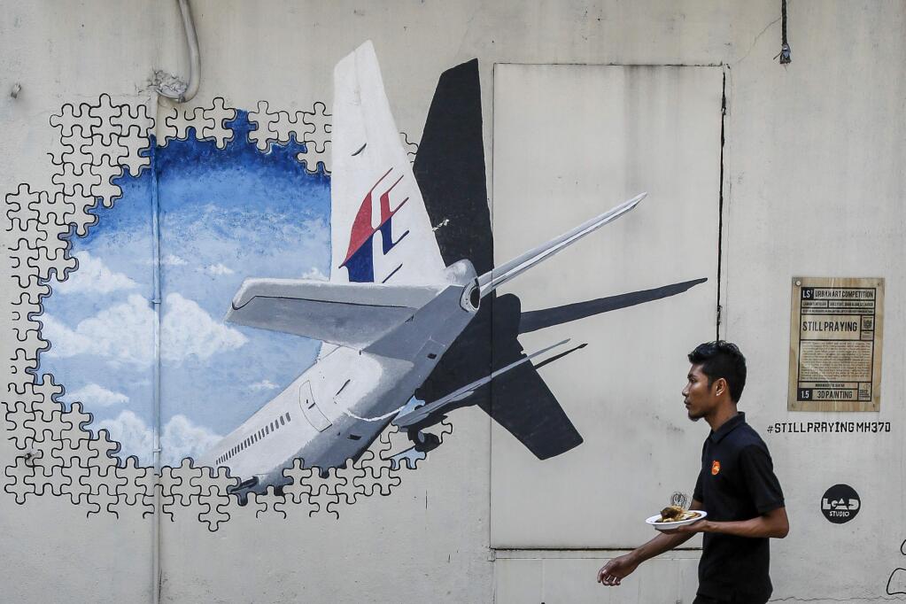 FILE - In this Tuesday, Feb. 23, 2016 file photo, a waiter walks past a mural of flight MH370 in Shah Alam outside Kuala Lumpur, Malaysia. South African authorities say debris found on a beach in Mozambique by a South African teenager will be sent to Australia to confirm if it is be part of missing Malaysia Airlines Flight 370, it was reported on Friday, March 11, 2016. (AP Photo/Joshua Paul, File)