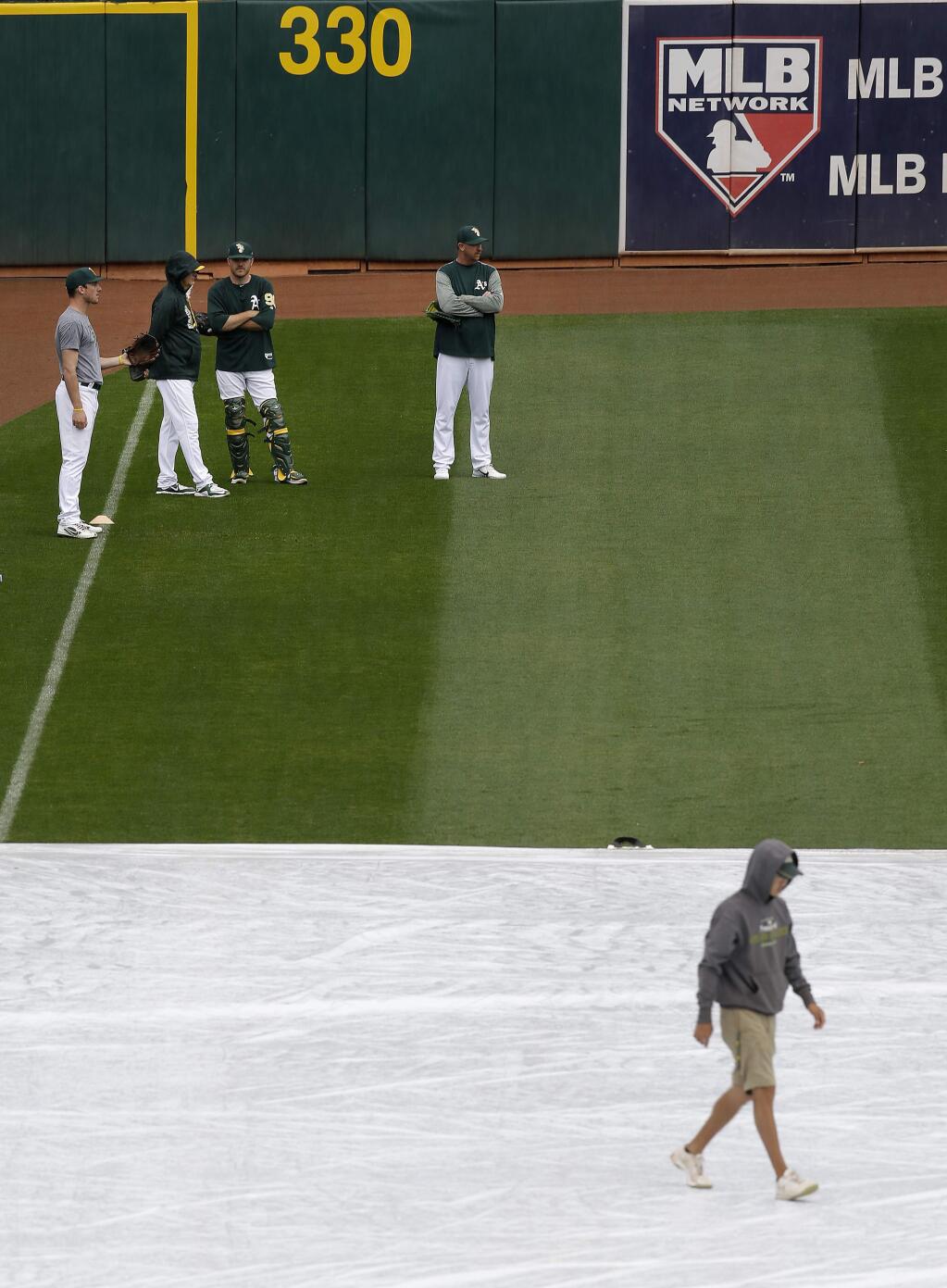 Oakland Athletics players prepare for Sunday's game against the Houston Astros as a groundskeeper walks on a tarp covering the infield. The game was eventually rained out. (AP Photo/Ben Margot)