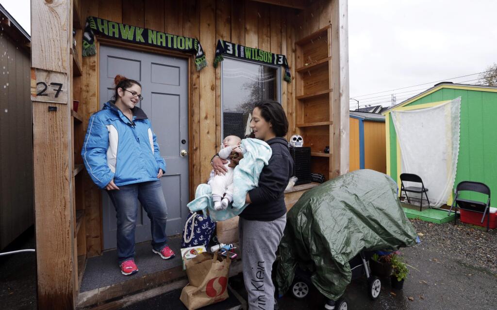 In this photo taken Thursday, Nov. 9, 2017, Eva Stough, right, holds her baby Kaysen Griffin, three months, as she returns to her tiny house where a neighbor greets her at a homeless encampment in Seattle. Tiny homes could be the solution to all kinds of housing needs, offering warmth and security for the homeless, an affordable option for expensive big cities and simplicity for people who want to declutter their lives. However, that seemingly broad support fails to translate into acceptance when tiny home developers try to build next door. (AP Photo/Elaine Thompson)