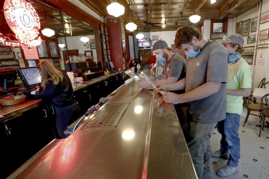 Construction workers Jacob Mooney, center, Corey Bowman, left, and Jason Mooney, right, look over menus at the 'Original Oyster House,' before ordering fish sandwiches during this year's '1-4-3 Day,' Friday, May 22, the 143rd day of 2020, in Pittsburgh. In 2019, Pennsylvania Gov. Tom Wolf declared May 23, 2019, the first '1-4-3 Day,' as a day of kindness in honor of Public Broadcasting Service's Fred Rogers, the host of children's program 'Mister Rogers' Neighborhood.' Rogers, a Pennsylvania native who died in 2003, used 143 as his special code for 'I Love You,' based on the number of letters in each word. For their part, the restaurant pledged that for every fish sandwich sold, $2 is going to be donated to The American Heart Association. (AP Photo/Keith Srakocic)