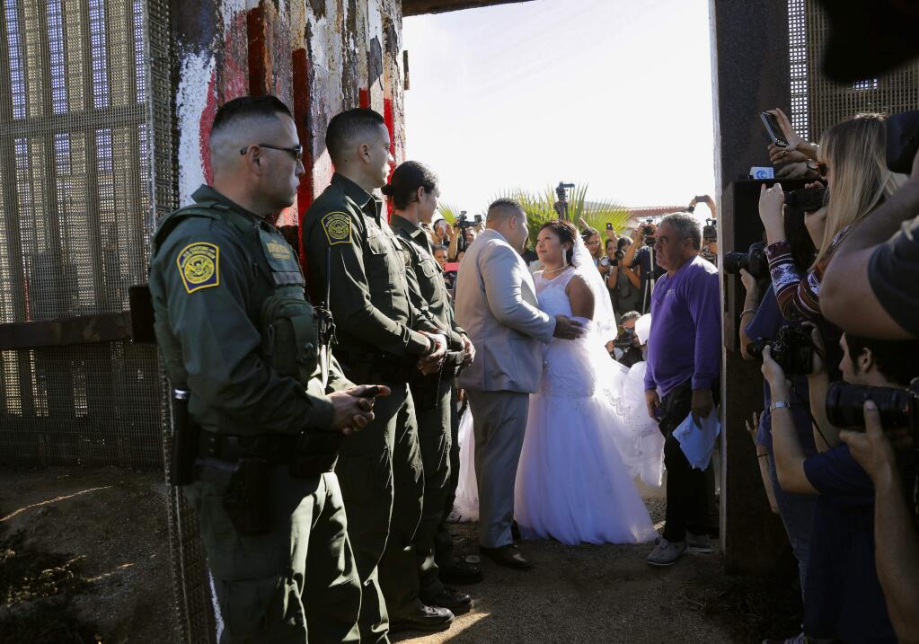 In this Saturday, Nov. 18, 2017, photo, Brian Houston, of Rancho San Diego, center left, and Evelia Reyes, right, of Tijuana, Mexico, look at each other in their wedding at the 'Door of Hope,' part of the border fence between the U.S. and Mexico. The United States man and the Mexican woman wedded Saturday between the doors of a steel border gate that opens for only an hour or so every year. Their wedding in San Diego was the first for an opening of the gate known as the Door of Hope. (Howard Lipin//The San Diego Union-Tribune via AP)