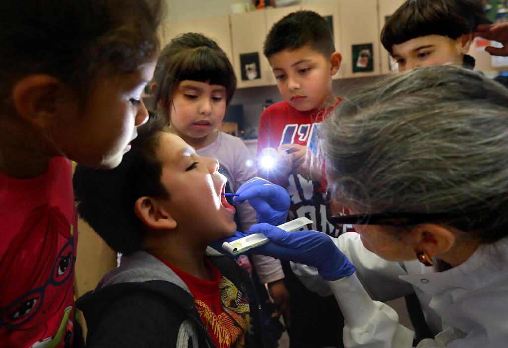 Volunteer dentist Gina Fontana applies a fluoride varnish treatment to the teeth of transitional kindergartener Allan Valencia while his classmates act as assistants at Brook Hill Elementary School in Santa Rosa on Friday, February 17, 2017. (John Burgess/The Press Democrat)