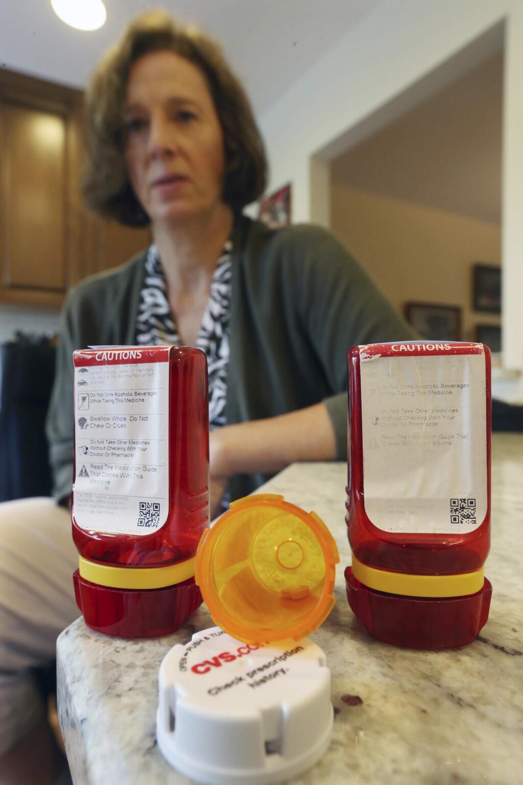 In this Sunday, Sept. 18, 2016, photo, Shelley Ewalt sits in her home, in Princeton, N.J., near an open amber-colored CVS pharmacy prescription bottle, center, and two uniquely designed red ones from Target. After CVS took over operation of Target's drugstores earlier this year, distraught customers have been asking the drugstore chain to bring back the retailer's red prescription bottles, which came with color-coded rings, labeling on the top and prescription information that was easier to read. Ewalt tweeted to the drugstore chain, asking if there was any chance they might return to the design of the Target bottles, which she found easier to open. (AP Photo/Mel Evans)