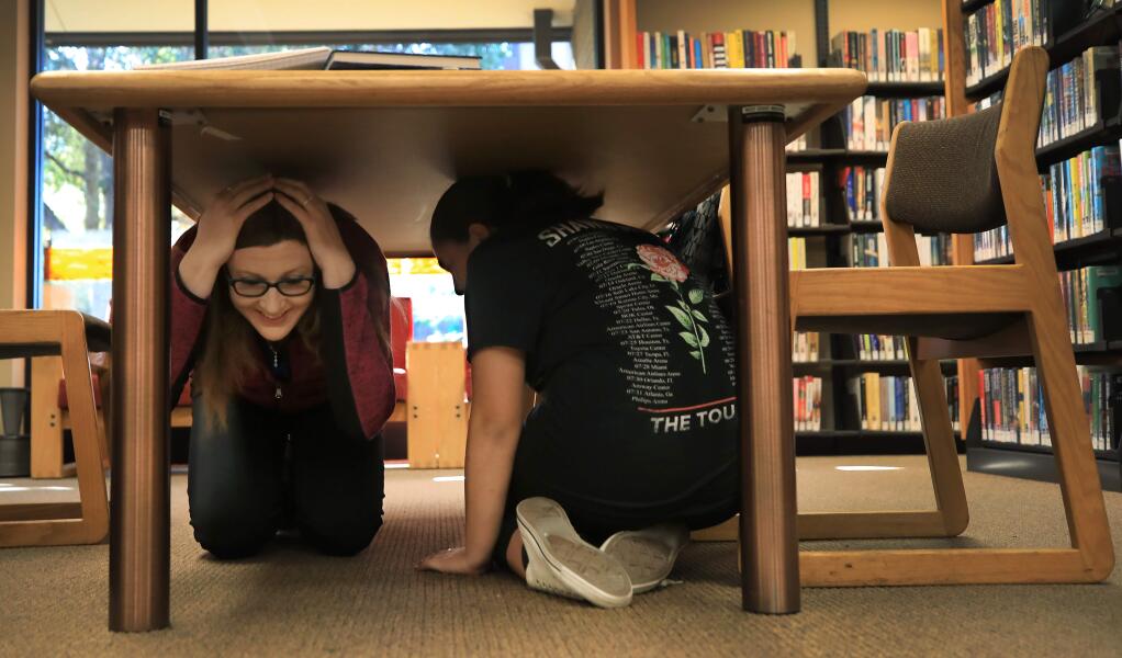 Independent studies instructor Laura McCorkell, left and student Jamie Onate, 13, duck and cover during the Great California Shakeout, Thursday, Oct. 17, 2019 at the Rincon Valley Regional Library in Santa Rosa. (Kent Porter / The Press Democrat)