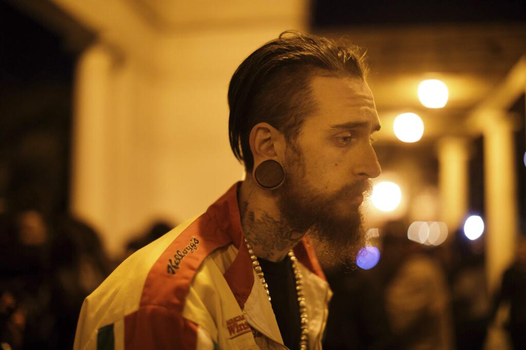 In this Dec. 5, 2016 photo, Max Harris, 27, who considers himself the 'creative director' or 'camp counselor' at the Oakland warehouse 'Ghost Ship' recounts the night of the fire during an interview at Lake Merritt, where a vigil for the fire victims was held in Oakland, Calif. A source close to the investigation tells The Associated Press Monday, June 5, 2017, that two men have been arrested and will be charged with involuntary manslaughter in the Ghost Ship warehouse fire that killed 36 partygoers. (Dai Sugano/San Jose Mercury News via AP)