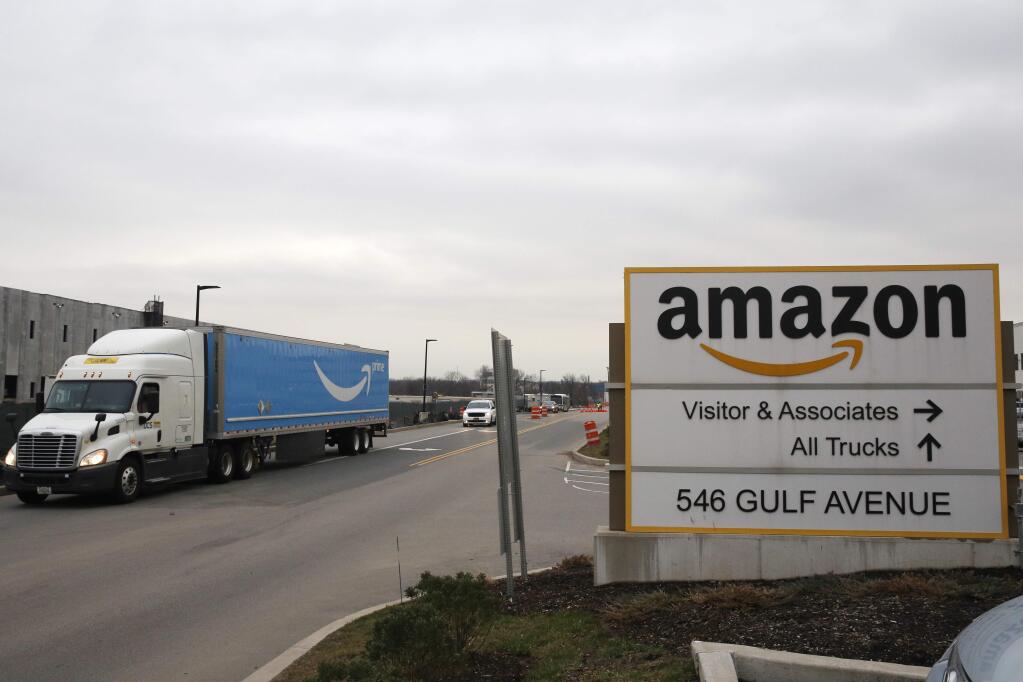 An Amazon Prime truck passes by a sign outside an Amazon fulfillment center, Thursday, March 19, 2020, on Staten Island, in New York. The company plans to add fulfillment and distribution center positions to keep up with increased demand during the coronavirus outbreak. (AP Photo/Kathy Willens)