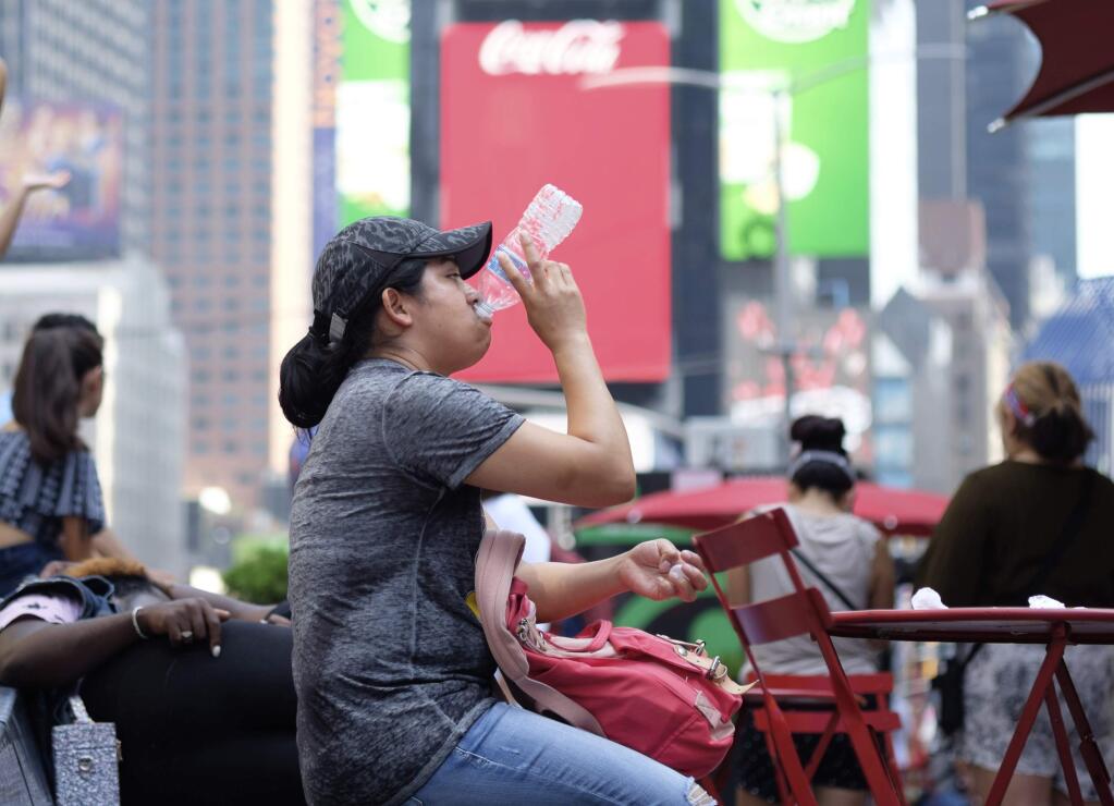 A woman drinks water in Times Square as temperatures reach the mid-to-upper 90s Saturday, July 20, 2019, in New York. Americans from Texas to Maine sweated out a steamy Saturday as a heat wave spurred cancelations of events from festivals to horse races and the nation's biggest city ordered steps to save power to stave off potential problems. (AP Photo/Jonathan Carroll)