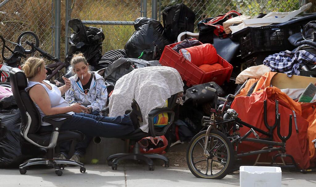 Occupants of the homeless camp on Sixth Street in Santa Rosa wait as city crews clean the underpass. The belongings in the background belong to several others. (Kent Porter / The Press Democrat) 2017