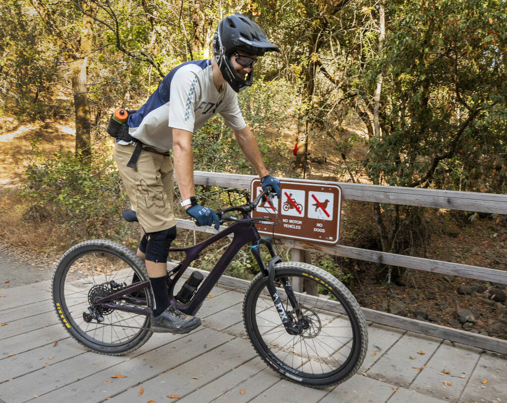 Garrett Thompson rides his Levo SL e-mountain bike past a no motor vehicles sign at Trione-Annadel State Park on Tuesday, Aug. 17, 2021. E-bikes are not allowed on trails in the park, but with a lack of park rangers to enforce the rules the number of battery powered bikers has increased with their popularity. (John Burgess/The Press Democrat)