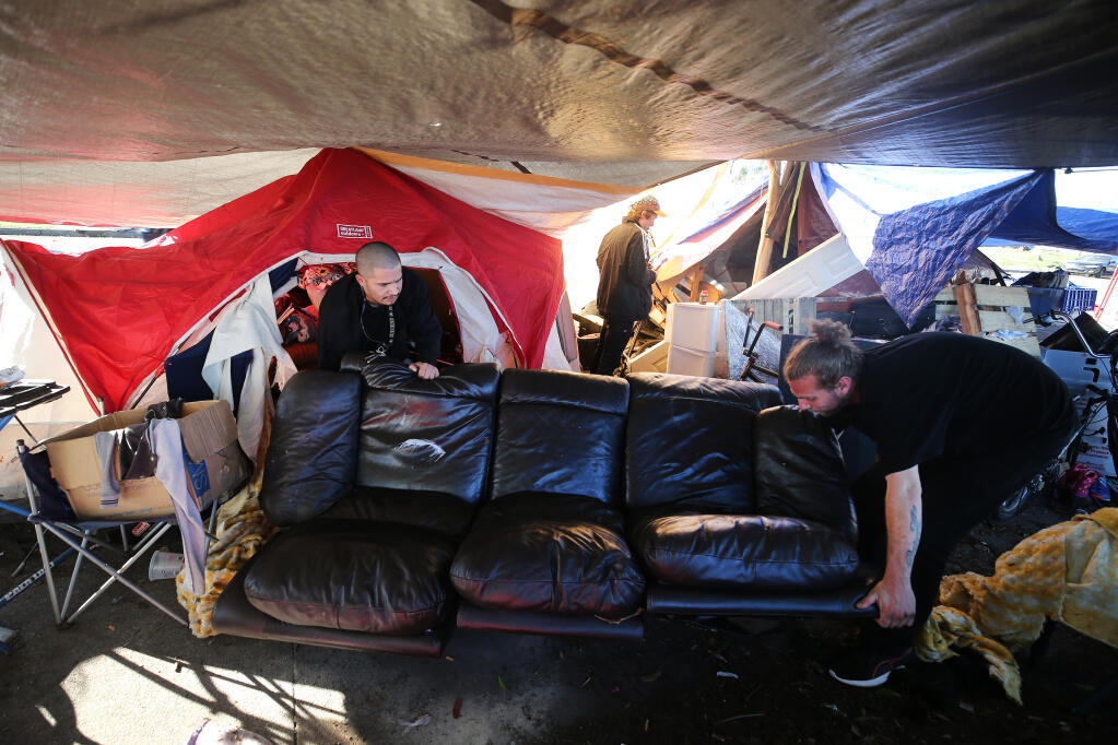 Homeless men Richard, left, and Brian, who wished not to give their last names, work to move a couch out of a tent at the homeless encampment on Industrial Drive in Santa Rosa, Calif., on Monday, Jan. 18, 2021. (Beth Schlanker / The Press Democrat)