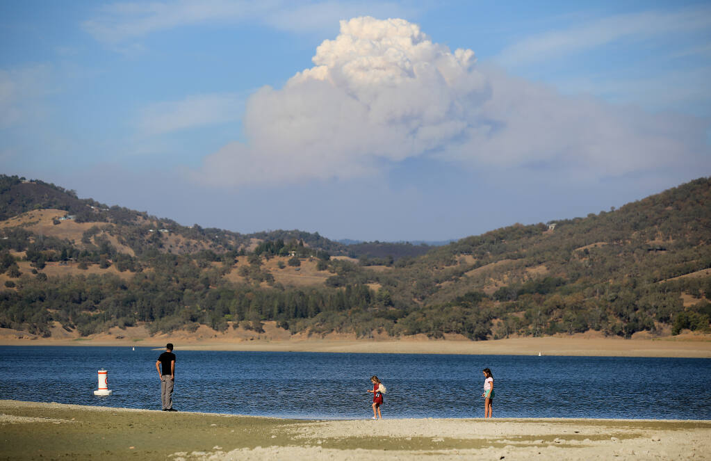 Vince Sims of Willits takes a walk with his daughters Stella, 7, Izabella, 11, on the drought-baked shoreline on Lake Mendocino's south end, Monday, August 21, 2020.  In the background is the August Complex fire.   (Kent Porter / The Press Democrat)