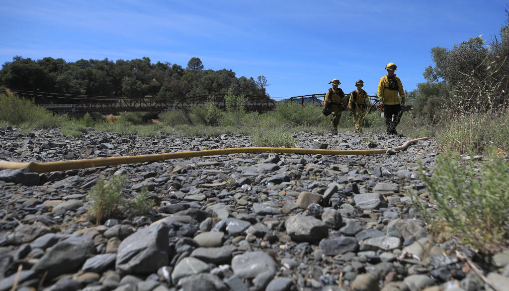 Firefighters use a Russian River gravel bar to walk to a 3-acre riverbank fire in Cloverdale, Saturday, June 5, 2021. (Kent Porter / The Press Democrat)