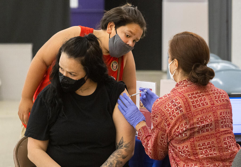 Skylark Ponce, 10 watches R.N. Cheryl Leighton give a COVID vaccine to his mother, Lugene Vanalst, at a Spanish-language vaccine event at Roseland vaccination clinic on Friday, Oct. 1, 2021. (John Burgess / The Press Democrat)