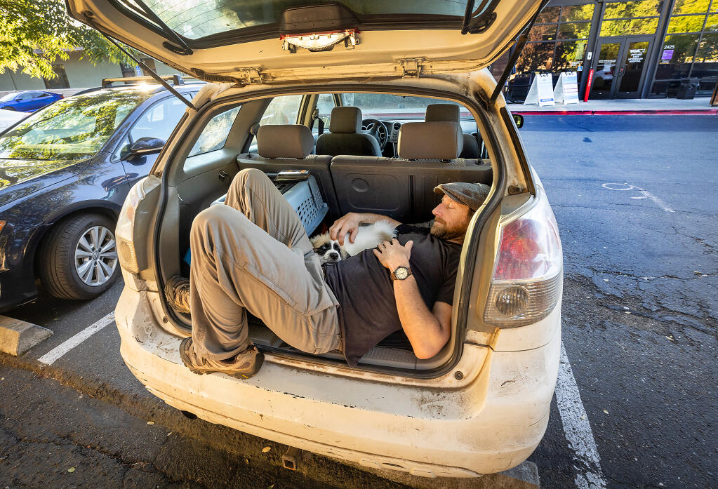 Will Egan rests in the back of his car with his 9-week-old Great Pyrenees puppy Bandit, waiting for emergency care in the parking lot of  VCA PetCare East Animal Hospital at sunset Tuesday, July 11, 2023 in Santa Rosa. After he was told there were no emergency vets in Mendocino county, Will drove from Pt. Arena in Mendocino, a 5-hour round-trip.(Photo John Burgess/The Press Democrat)