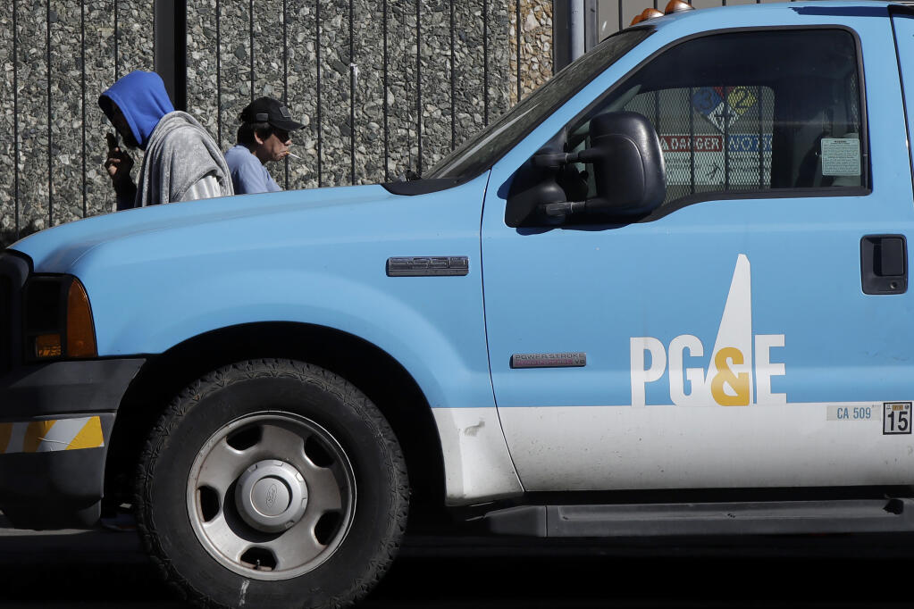 FILE - People walk behind a Pacific Gas and Electric truck parked in San Francisco, Tuesday, Feb. 18, 2020. Pacific Gas & Electric on Wednesday, May 26, 2021 got socked with a nearly $150 million bill for its neglectful role in causing Northern Calfirowill pay $43.4 million to government agencies in three Northern California counties to cover bills left behind from wildfires ignited during the past two years by the beleaguered utility's long-neglected power grid. (AP Photo/Jeff Chiu)