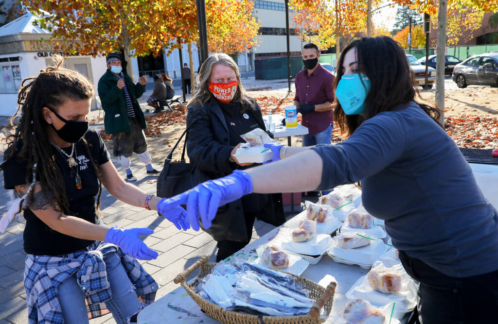 Sonoma County Acts of Kindness volunteers Zoe Kessler, right, and Lisa Aldana, right, help Jenny Schultz with her Thanksgiving meal at Old Courthouse Square in Santa Rosa on Thursday, Nov. 26, 2020. (Christopher Chung/ The Press Democrat)