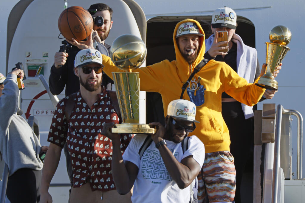 The Golden State Warriors, including Stephen Curry, holding his NBA Finals MVP trophy; Klay Thompson, left; and Draymond Green, holding the Larry O'Brien Championship Trophy, step off a plane at San Francisco International Airport on Friday, June 17, 2022, in San Francisco. The Warriors returned from Boston as NBA champions after defeating the Celtics in six games. (Santiago Mejia/San Francisco Chronicle via AP)