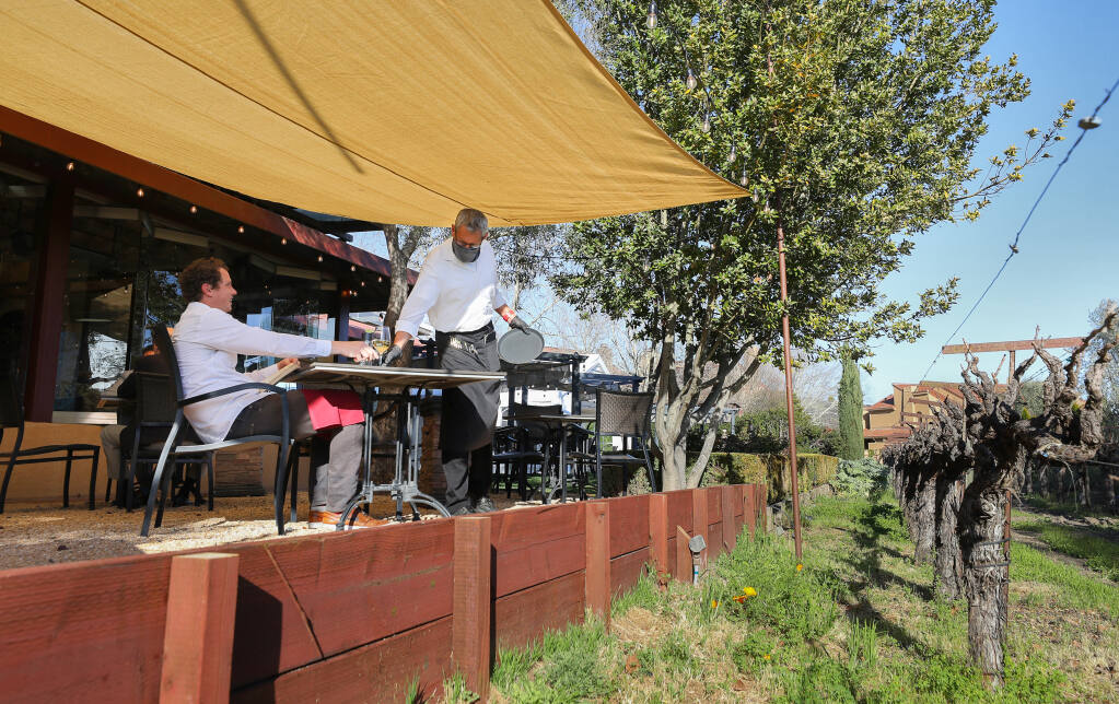 Alan Luzmoor, right, serves a glass of wine to Duncan Lish at the John Ash & Co. restaurant in Santa Rosa on Tuesday, March 23, 2021. An herb garden was removed to make way for the outdoor dining area to accommodate for dining restrictions due to the coronavirus pandemic.  (Christopher Chung/ The Press Democrat)