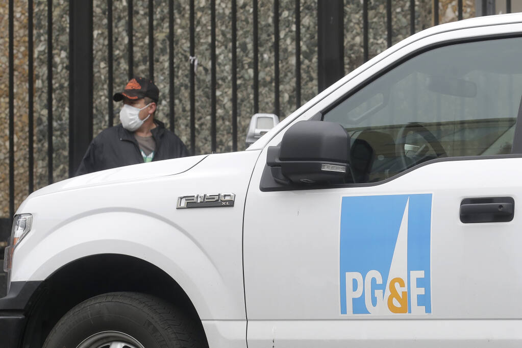 In this April 16, 2020, file photo, a man wearing a mask walks behind a Pacific Gas and Electric truck in San Francisco. (AP Photo/Jeff Chiu)