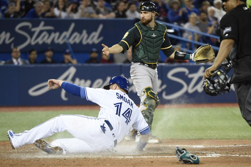 Toronto Blue Jays' Justin Smoak (14) slides into home plate to score a run as Oakland Athletics catcher Jonathan Lucroy (21) stands nearby during the fifth inning of a baseball game Thursday, May 17, 2018, in Toronto. (Nathan Denette/The Canadian Press via AP)