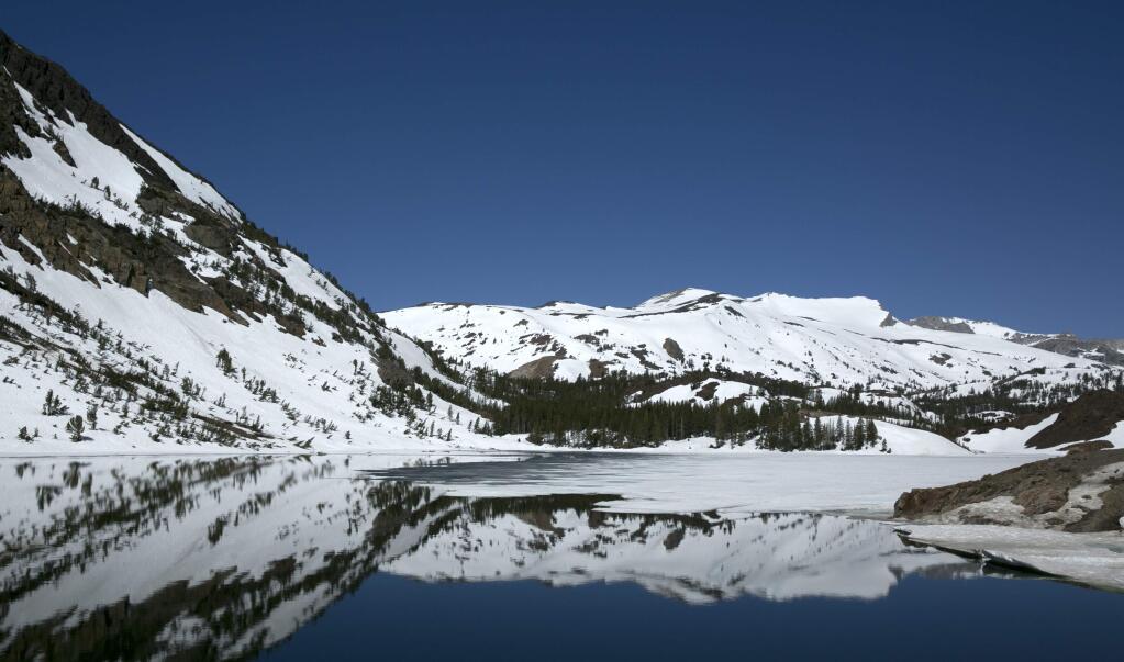 In this photo taken Tuesday, June 6, 2017, snow capped mountains are reflected by Ellery Lake near Yosemite National Park, Calif. This year's heavy snowfall has kept Highway 120 closed longer then normal, preventing visitors to the area from taking in the scenery. Crews are working overtime to clear snow from the only road through Yosemite as summer approaches, which connects the Central Valley on the west side with the Owens Valley on the east side of the Sierra Nevada. (AP Photo/Rich Pedroncelli)