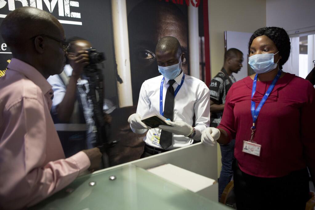 A traveller has his passport checked by staff wearing masks at Robert Mugabe International airport in Harare, Wednesday, March, 11, 2020. For most people, the new coronavirus causes only mild or moderate symptoms, such as fever and cough. For some, especially older adults and people with existing health problems, it can cause more severe illness, including pneumonia. (AP Photo/Tsvangirayi Mukwazhi)