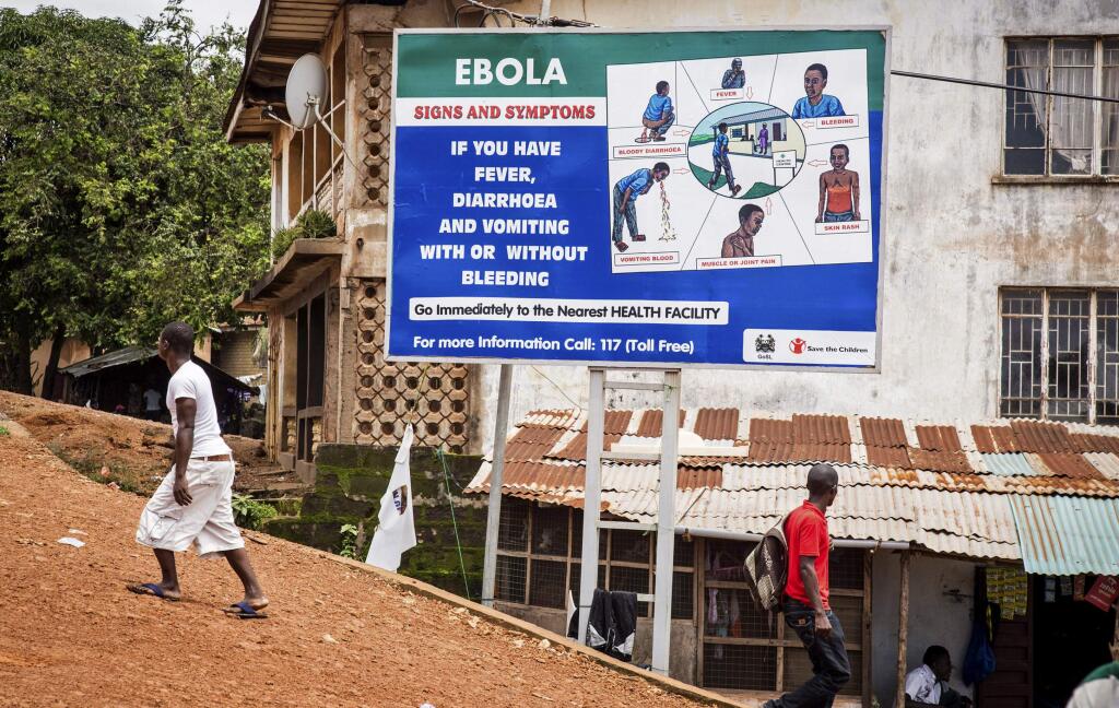 People walk past a billboard encouraging people suffering from symptoms linked to Ebola to present themselves at a health facility for treatment in Freetown, Sierra Leone, Thursday, Aug. 7, 2014. While the Ebola virus outbreak has now reached four countries, Liberia and Sierra Leone account for more than 60 percent of the deaths, according to the World Health Organization. The outbreak that emerged in March has claimed at least 932 lives. (AP Photo/ Michael Duff)