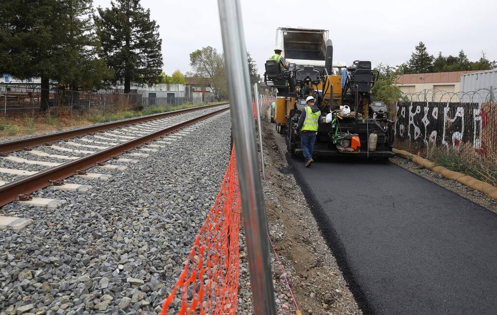 A construction crew paves an asphalt pedestrian pathway alongside the SMART tracks, near Southpoint Boulevard, in Petaluma on Friday, September 27, 2019. (Christopher Chung/ The Press Democrat)