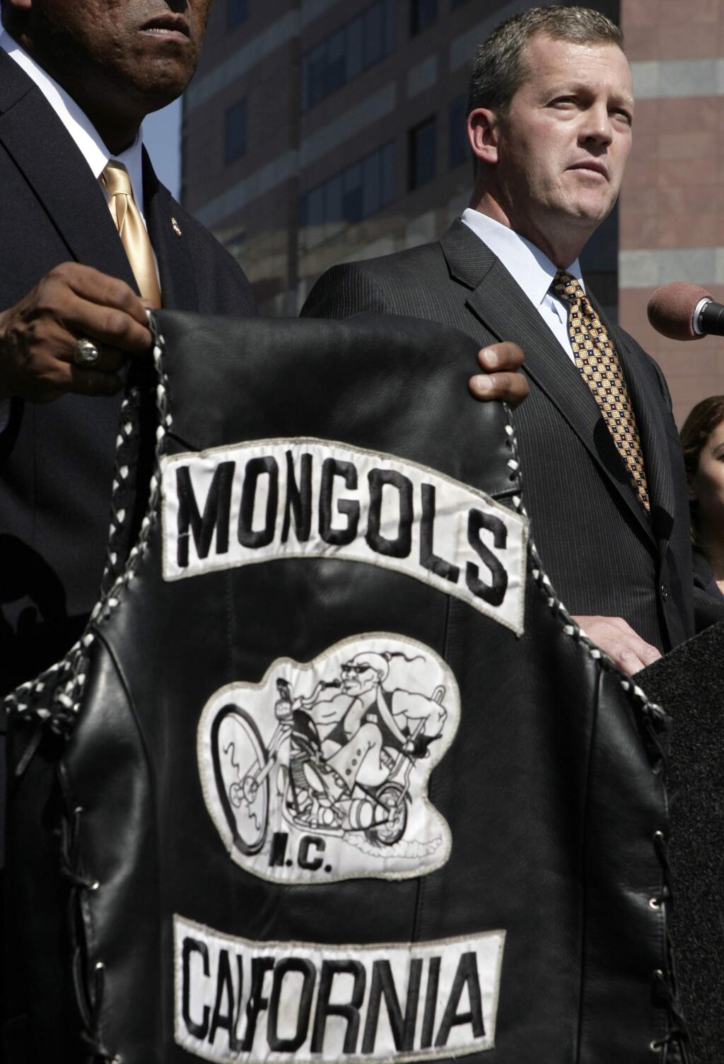 FILE - In this Tuesday, Oct. 21, 2008 file photo, U.S. Attorney Thomas P. O'Brien, right, speaks during a news conference in Los Angeles about the arrest of several Mongol motorcycle gang members in six states as a vest with the Mongols logo displayed. Federal prosecutors say a California jury has decided the Mongols motorcycle gang should be stripped of its trademarked logo. Jurors in U.S. District Court in Santa Ana on Friday, Jan. 11, 2018, found that the government could seize control of the group's trademark. The jury previously found the Mongol Nation, the entity that owns the image of a Mongol warrior on a chopper, guilty of racketeering and conspiracy. (AP Photo/Ric Francis, File)