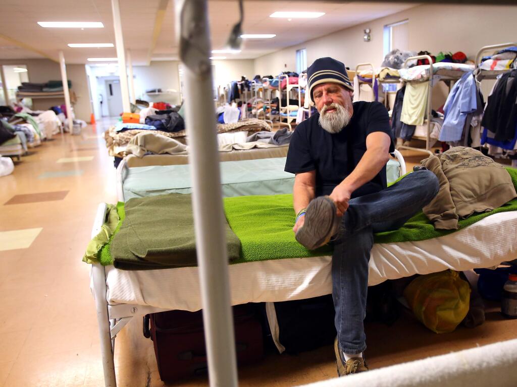 Chris Alexander pulls on his shoes at his cot in the Samuel L. Jones Hall Shelter, operated by Catholic Charities, in Santa Rosa on Monday, January 6, 2014. (Christopher Chung/ The Press Democrat)