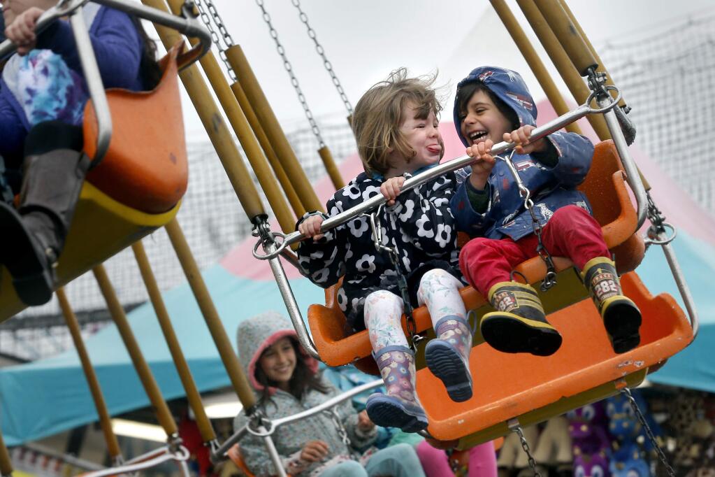 Abby Kruger, 4, sticks her tongue out at Maceo Loarie, 5, as they ride the swings in the rain at the Citrus Fair in Cloverdale, on Sunday, February 19, 2017. (BETH SCHLANKER/ The Press Democrat)