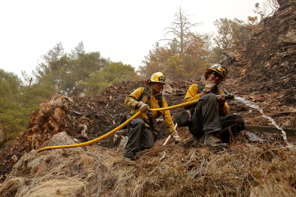 Firefighters Clyde Rust, left, and Julien Lecorps make a progressive hose lay in rugged terrain to extinguish hot spots from the Nuns fire near homes around Hood Mountain Regional Park in Santa Rosa, California on Monday, October 16, 2017. (Alvin Jornada / The Press Democrat)
