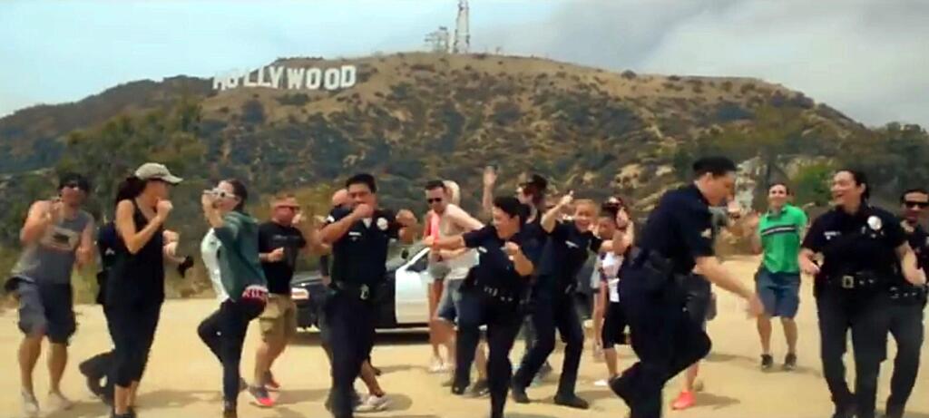 In this undated frame from video provided by the Los Angeles Police Department, LAPD officers and others dance beneath the iconic Hollywood Sign in Los Angeles. In a now-viral sensation, police officers across the U.S. are dancing an updated version of the running man to a catchy 1990s hip hop song, 'My Boo' by Ghost Town DJ's, in videos that have included professional sports mascots, cheerleading squads and at least one explosion. The videos started with the New York Police Department and are getting more elaborate and popular, with even some police chiefs joining in. (Los Angeles Police Department via AP) MANDATORY CREDIT