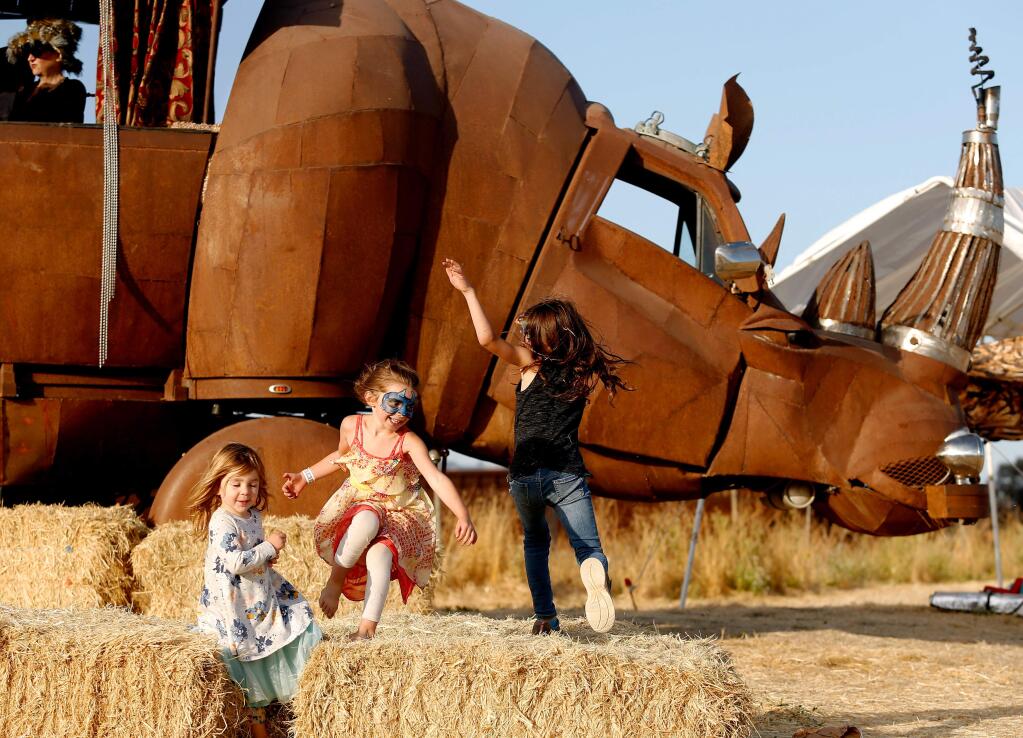 Scarlett Beaver, 5, center, chases her sister Riley, 8, in front of the Rhino Redemption art car while their cousin Evie Jirout, 2, left, looks on, during Rivertown Revival at Steamer Landing Park in Petaluma, California, on Saturday, July 14, 2018. (Alvin Jornada / The Press Democrat)