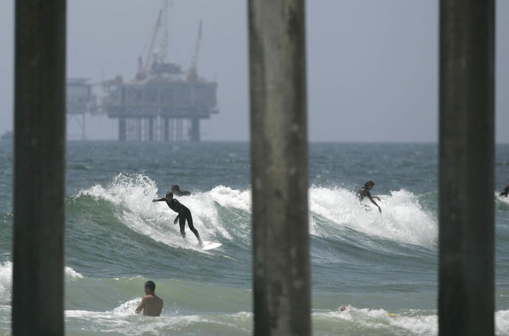 Surfers and swimmers share the waves near the Huntington Beach Pier while an offshore oil rig stands in the background. (ADAM LAU / Associated Press, 2010)