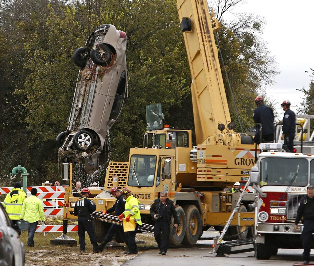 A car is taken out of a sinkhole in San Antonio, Monday, Dec. 5, 2016. A city official said a 60-year-old man was rescued after two cars were submerged inside a sinkhole created when a large sewer line ruptured. (Ron Cortes/The San Antonio Express-News via AP)