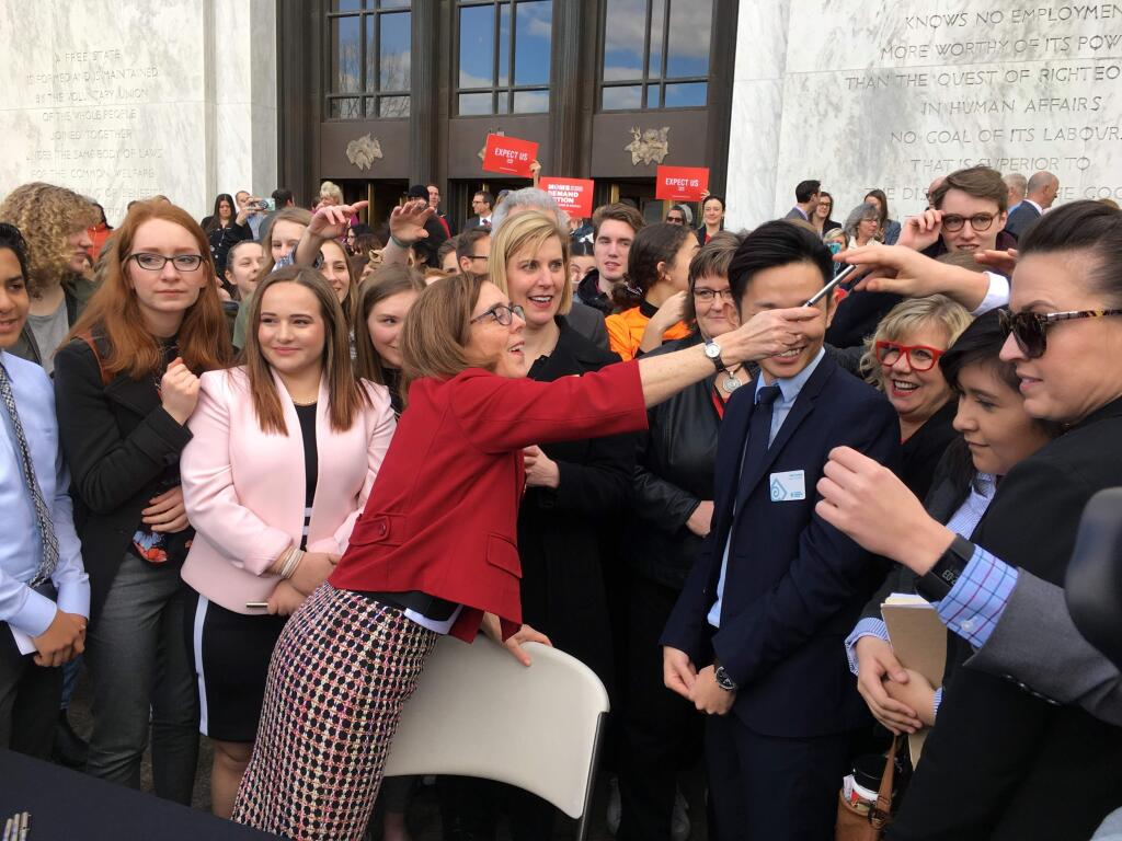 Oregon Gov. Kate Brown hands out one of the pens that she used to sign the first gun-control legislation signed into law in America since the Valentine's Day massacre at a Florida high school, on the steps of the state Capitol in Salem, Ore., Monday, March 5, 2018. Oregon high school students were among those who observed the signing. (AP Photo/Andrew Selsky)