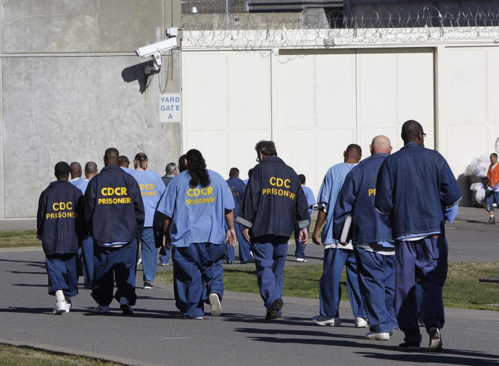 FILE - In this Feb. 26, 2013, file photo, inmates walk through the exercise yard at California State Prison Sacramento, near Folsom, Calif. One inmate and five employees in California's massive prison system have tested positive for coronavirus, leading to increased pressure Monday, March 23, 2020, on corrections officials to begin releasing some of the state's 123,000 convicts early. (AP Photo/Rich Pedroncelli, File)