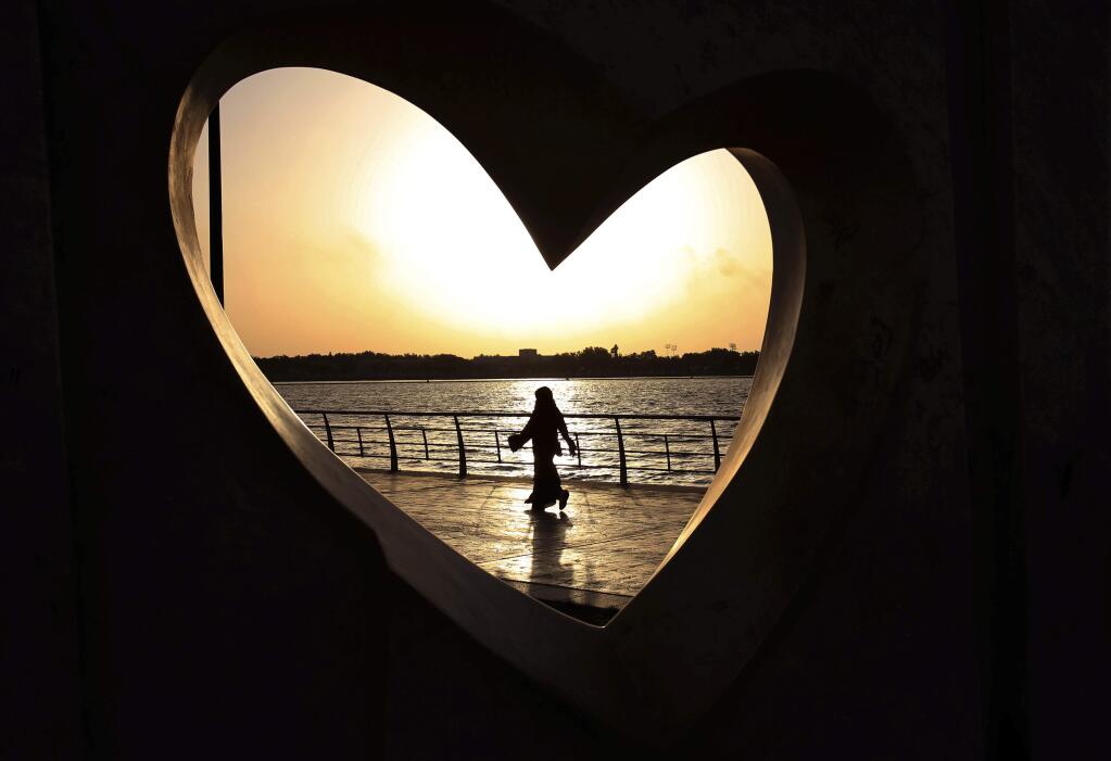 FILE -- In this May 11, 2014 file photo, a Saudi woman seen through a heart-shaped statue walks along an inlet of the Red Sea in Jiddah, Saudi Arabia. A young Saudi woman has sparked a sensation online by posting a video of herself in a miniskirt and crop top walking around in public, with some Saudis calling for her arrest and others rushing to her defense. The video, first shared on Snapchat, shows her walking around an empty historic fort in Ushaiager, a village north of the capital, Riyadh, in the desert region of Najd, where many of Saudi Arabia's most conservative tribes and families are from. (AP Photo/Hasan Jamali, File)