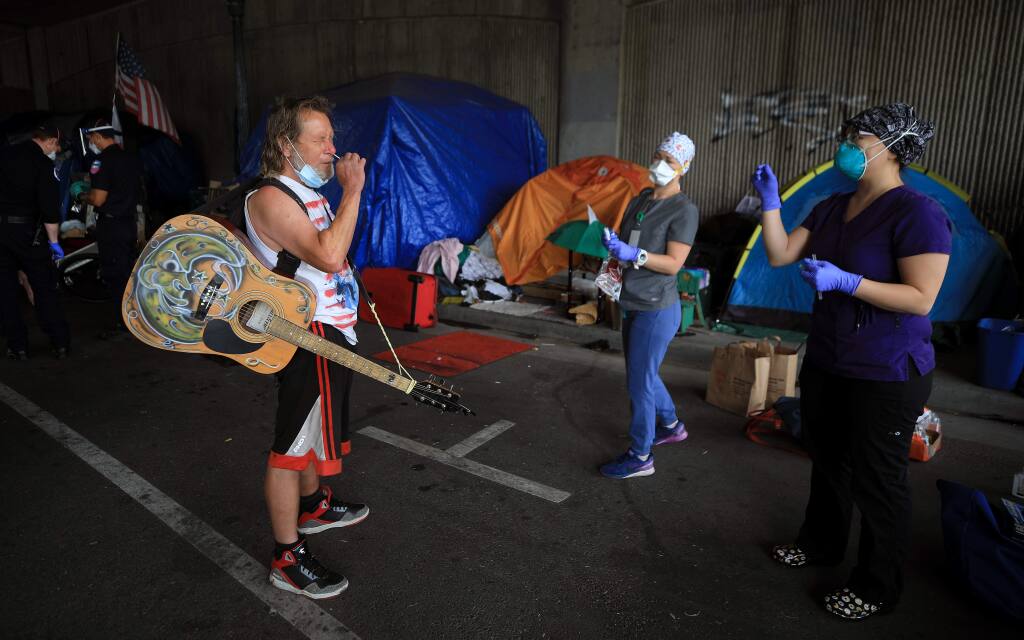 Billy Blankenship is coached by Sandra Castano, right, and Amy Bradbury from the Petaluma Health Center as Blankenship takes a swab test for the coronavirus at the Sixth Street homeless camp in Santa Rosa, Saturday, June 20, 2020. (Kent Porter / The Press Democrat) 2020