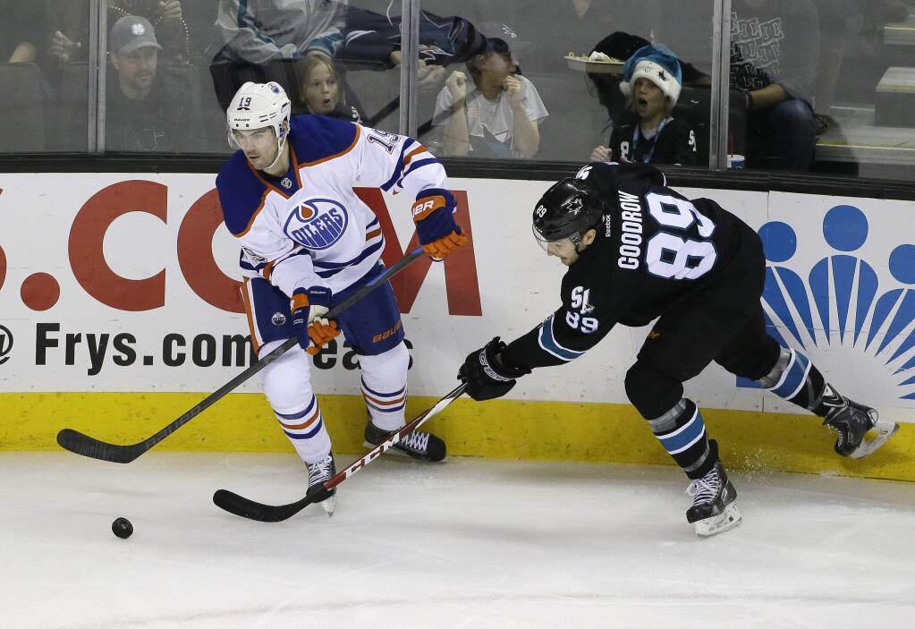 Edmonton Oilers defenseman Justin Schultz, left, and San Jose Sharks left wing Barclay Goodrow, right, reach for the puck during the first period of a game Thursday, Dec. 18, 2014, in San Jose. (AP Photo/Eric Risberg)