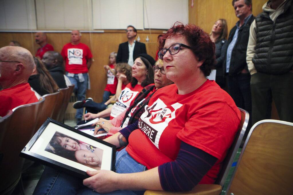 Adriann Saslow who lives across the street from the proposed Safeway gas station in East Petaluma, listens to speakers during City Council where the public was invited to comment. Adriann spoke about the suspected dangers to her family including her two children, Miriam,3, and Derek, 16 months, whose picture she holds. (CRISTINA PASCUAL/ARGUS-COURIER STAFF)