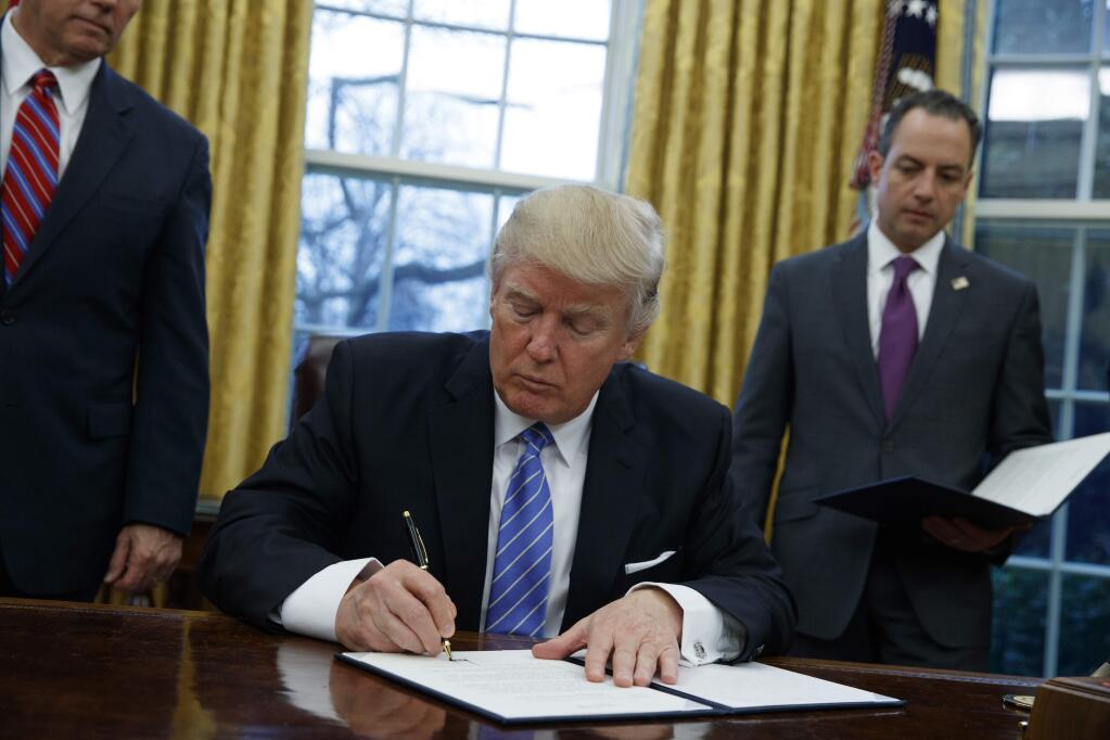 President Donald Trump signs an executive order to withdraw the U.S. from the 12-nation Trans-Pacific Partnership trade pact agreed to under the Obama administration, Monday, Jan. 23, 2017, in the Oval Office of the White House in Washington. (AP Photo/Evan Vucci)