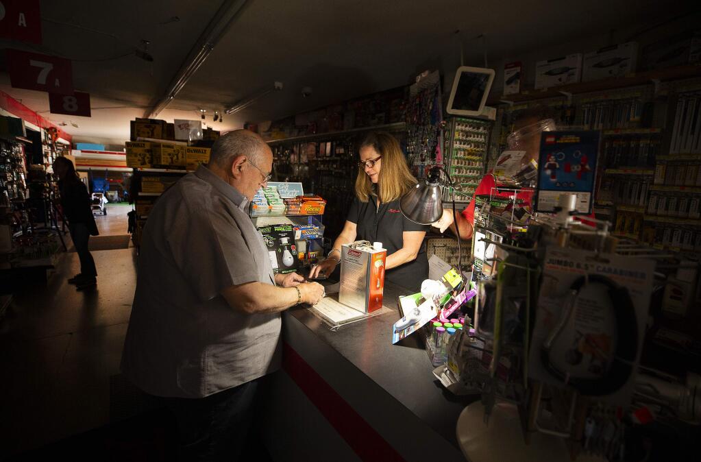 Tom Hyde picks up a can of fuel for his Coleman camp stove from Kim Scheffer at the Village True Value Hardware store in Santa Rosa on Wednesday, Oct. 9, 2019. The store used a generator to run a light, the register and a dial-up credit card machine to serve customers during the power outage. (JOHN BURGESS/ PD)