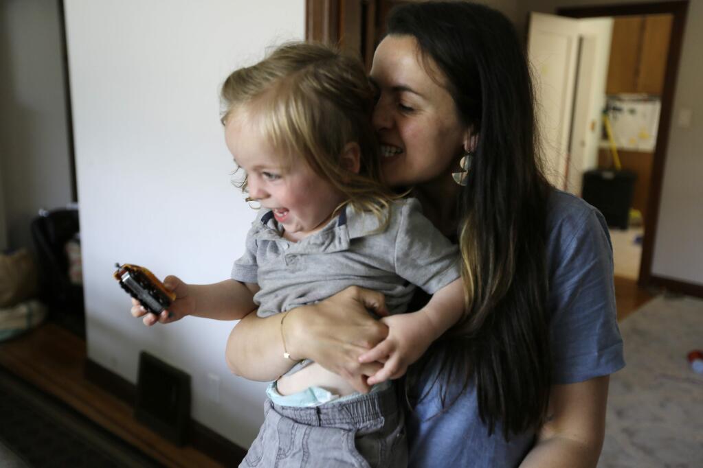 In this Thursday, June 6, 2019 photo, Sarah Montoya picks up her twin son, Nicasio, at their home in San Francisco. During last year's deadly Camp Fire, which killed 85 people and destroyed 14,000 homes, smoke from the blaze inundated a San Francisco neighborhood roughly 170 miles away where Montoya lives with her husband, Trevor McNeil, and their three children. All three children have respiratory problems suspected to be asthma. But when the smoke from the Camp Fire filled the air for two weeks, the family was unable to find child-sized face masks to protect them or an air filter to clear the air in their house. (AP Photo/Eric Risberg)
