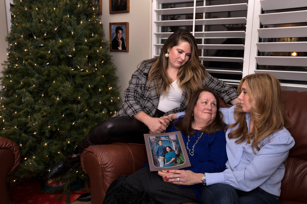 Maureen Minto, center, holds a cherished picture of herself with her son, Kirk Brandt, who died recently after a car accident, along with Kirk's two sisters, Alexa Brandt, top left, and Mariah Brandt, right, as they hold hands and celebrate Kirk's life at the family home, Friday, December 23, 2022, in Santa Rosa.  (Darryl Bush / For The Press Democrat)