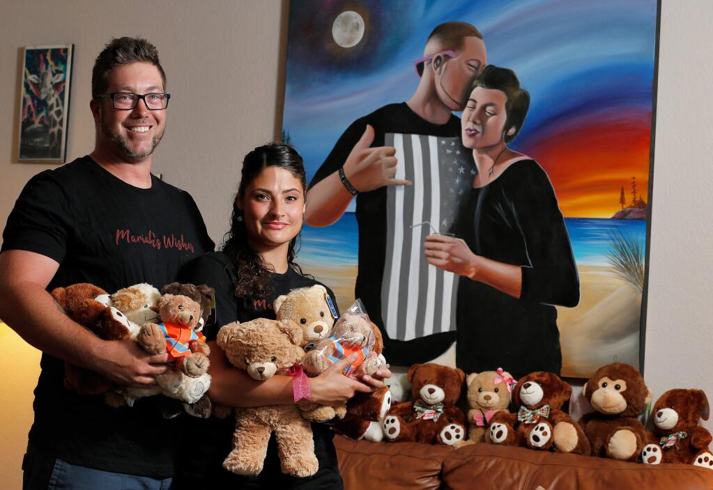 Chris Boblitt, left, and his girlfriend Mikaela Gannon pose for a portrait in front of a painting of Boblitt and his sister Mariah Roat, who inspired Boblitt to deliver teddy bears to hospitalized children after she died five years ago. Photographed at their home Petaluma, California, on Tuesday, July 30, 2019. (Alvin Jornada / The Press Democrat)