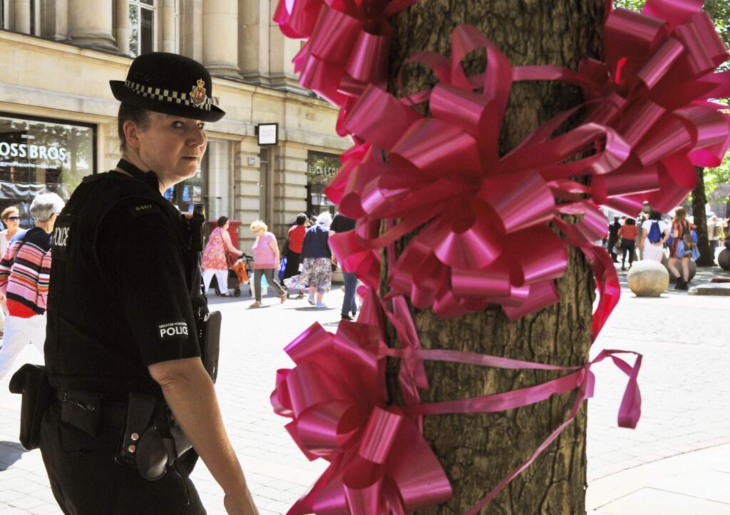 Police patrol past a pink ribbon tribute in central Manchester, England Friday May 26 2017. More than 20 people were killed in an explosion following a Ariana Grande concert at the Manchester Arena late Monday evening. (AP Photo/Rui Vieira)