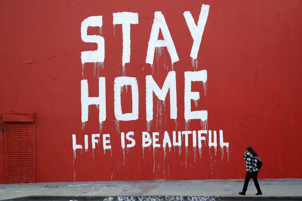 A Los Angeles pedestrian walks past a mural that 'Stay at Home, Life is Beautiful.' (MARCIO JOSE SANCHEZ / Associated Press)